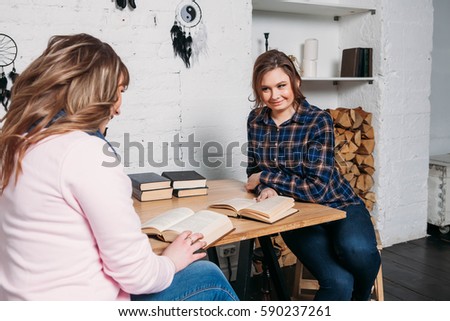 Two students doing homework together and helping each other sitting in a table at home with a homey background