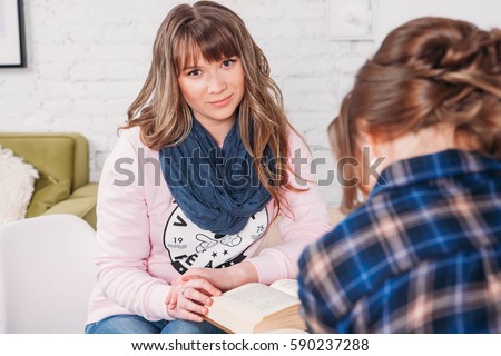 Two students doing homework together and helping each other sitting in a table at home with a homey background