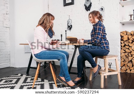 Two students doing homework together and helping each other sitting in a table at home with a homey background