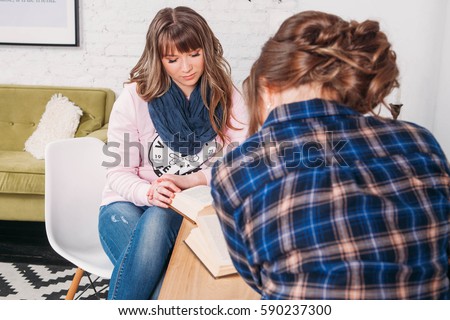 Two students doing homework together and helping each other sitting in a table at home with a homey background