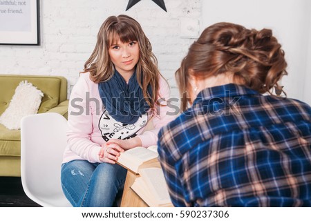 Two students doing homework together and helping each other sitting in a table at home with a homey background