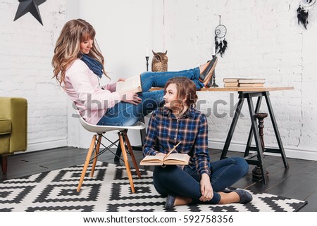 Two students doing homework together and helping each other sitting in a table at home with a homey background