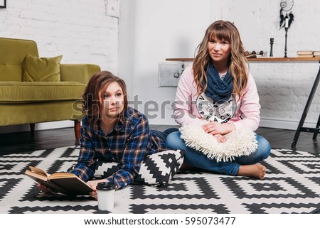 Two students doing homework together and helping each other lying on the floor at home with a homey background