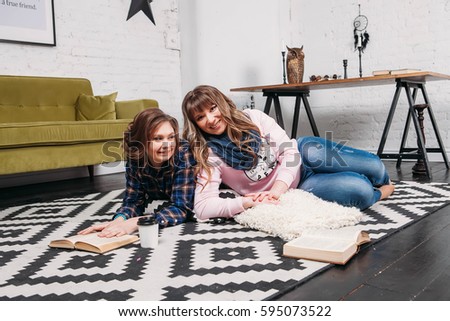 Two students doing homework together and helping each other lying on the floor at home with a homey background