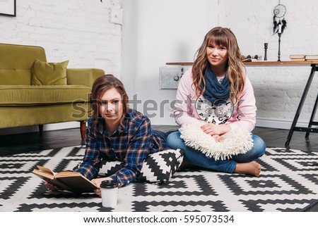 Two students doing homework together and helping each other lying on the floor at home with a homey background
