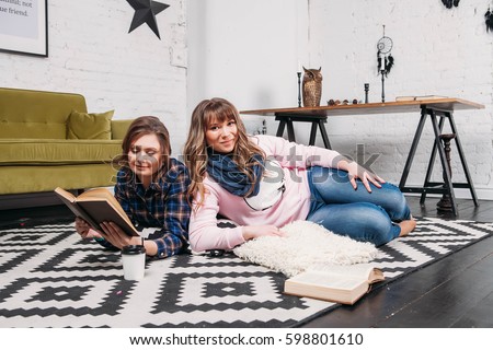 Two students doing homework together and helping each other lying on the floor at home with a homey background