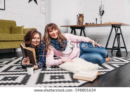 Two students doing homework together and helping each other lying on the floor at home with a homey background