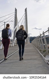 Two Students Girls With Backpacks Walking On Pedestrian Part Of Transportation Tilikum Crossing Bridge With Railway For Streetcar Across The Willamette River In Portland Oregon