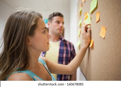 Two Students Looking At Notice Board  At College