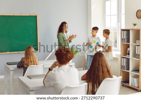 Two students presenting a project or classwork during a lesson with the teacher in a school classroom. This activity highlights studying, learning, and teamwork in educational environment.