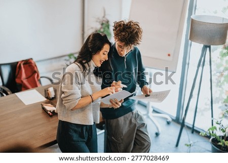 Two students study and review printed documents together while pointing at notes. The pair collaborate closely in a bright classroom setting, sharing ideas and feedback.