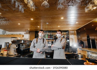 Two stylish bartenders in masks and uniforms during the pandemic, stand behind the bar. The work of restaurants and cafes during the pandemic.