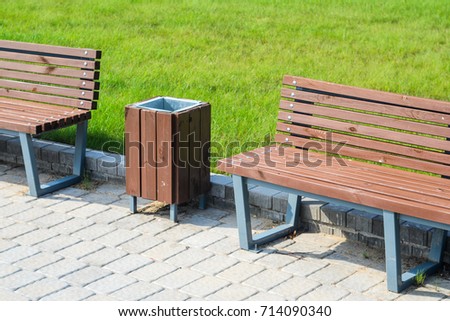 Two stylish benches and a trash can in a summer park along a paved path against a green lawn. Small architectural forms concept