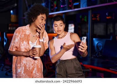 Two stylish interracial women sharing moment of joy and connection over coffee, looking at phone - Powered by Shutterstock