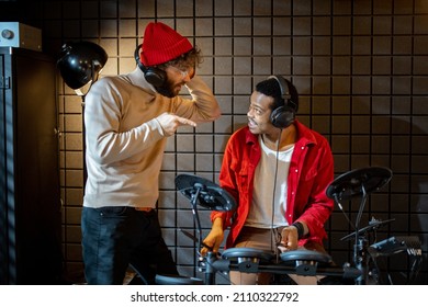 Two Stylish Men Playing Electric Drums, Composing Electronic Music At Small Recording Studio. Small Band Creating Or Practicing Music In A Home Studio. Caucasian And Hispanic Man Playing Together