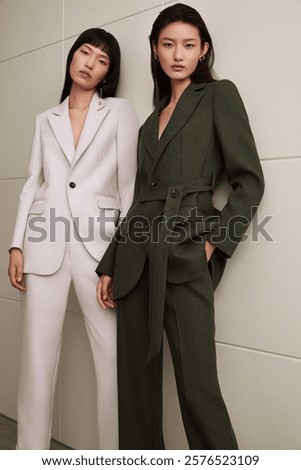 Two stylish models posing in tailored suits with neutral background.