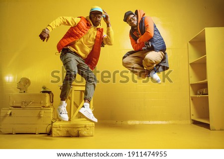 Two stylish rappers in studio, yellow background
