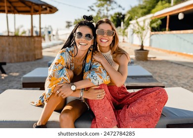 two stylish smiling beautiful women relaxing having fun on beach in summer fashion trend outfit, colorful apparel boho style, having tropical vacation wearing sunglasses - Powered by Shutterstock