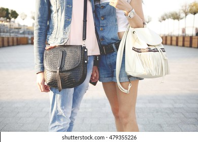 Two Stylish Women Legs In Blue Jeans And Shorts Holding Messenger Leather Bag And Backpack In Hand. Street Fashion Outfit