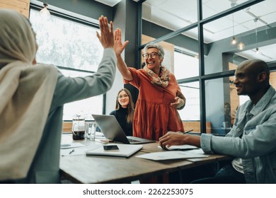 Two successful businesswomen high fiving each other during an office meeting. Cheerful businesswomen celebrating their achievement. Happy businesspeople working as a team in a multicultural workplace. - Powered by Shutterstock