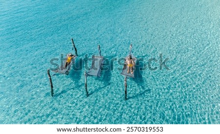 Two sunbathers lounge on floating hammocks, enjoying the serene turquoise waters of Koh Kood, Thailand. Sunlight sparkles on the surface, creating a tranquil atmosphere perfect for relaxation.