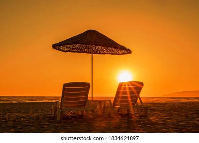 two sunbeds under big umbrella on sandy beach in sunset time back view