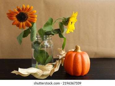 Two sunflowers in a mason jar. with one small orange pumpkin. With some dry leaves on a black wooden table. Brown paper bag colored background. - Powered by Shutterstock