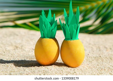 Two sunny easter eggs with pineapple leaves on the sandy beach near the ocean