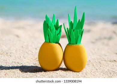 Two sunny easter eggs with pineapple leaves on the sandy beach near the ocean