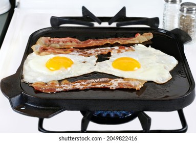 Two sunny side up eggs with bacon frying on a cast iron griddle, stove top with burner flame. - Powered by Shutterstock