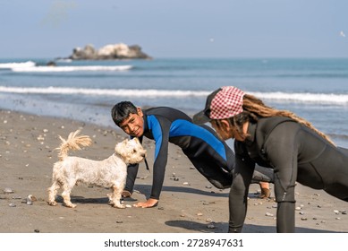 Two surf students in wetsuits performing warm up exercises on a sandy beach, preparing for a surfing lesson