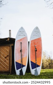 Two surfboards, accompanied by oars, are casually leaning against the side of a sturdy wooden shed, creating an inviting scene full of recreational potential and a love for the ocean