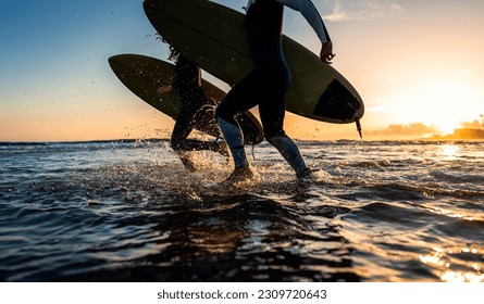 Two surfers with surfboard prepares to hit the waves at sunset. - Powered by Shutterstock