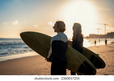 Two surfers with surfboard prepares to hit the waves at sunset. - Powered by Shutterstock