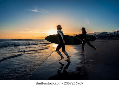 Two surfers with surfboard running at beach preparing to hit the waves at sunset. - Powered by Shutterstock