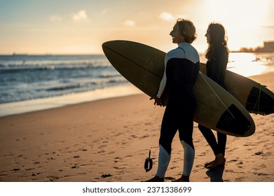 Two surfers with surfboard stnding on beach at sunset. - Powered by Shutterstock