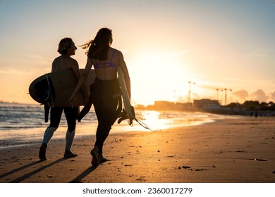 Two surfers with surfboard walking on beach at sunset. - Powered by Shutterstock