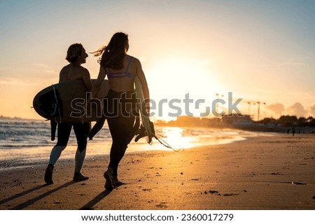 Two surfers with surfboard walking on beach at sunset.