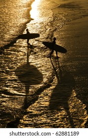 two surfers walking in silhouette on a beach.