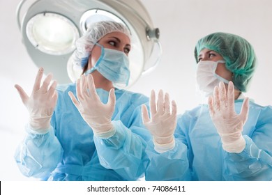 Two surgeons in coats,masks,caps and sterile gloves