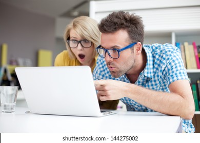 Two surprised students learning in library on laptop