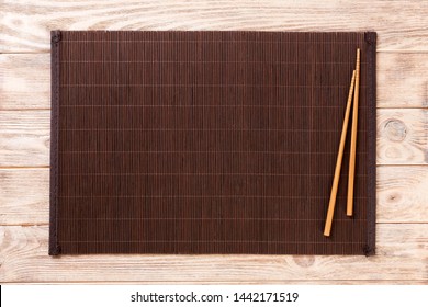 two sushi chopsticks with empty bamboo mat or wood plate on brown wooden Background Top view with copy space. empty asian food background.