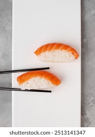 Two sushi nigiri with salmon on a white plate, chopsticks, close-up, conceptual and stylized