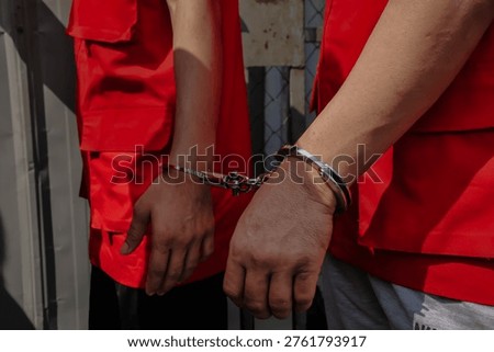 Two suspects in red vests handcuffed together during a legal investigation or criminal court proceeding.