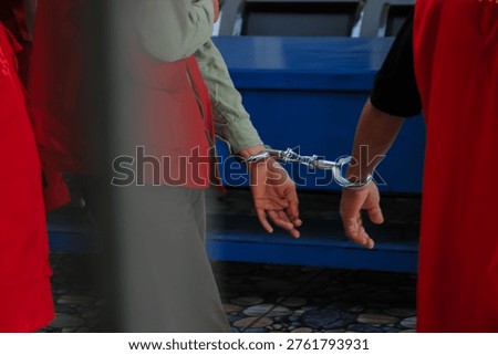 Two suspects in red vests handcuffed together during a legal investigation or criminal court proceeding.