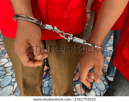 Two suspects in red vests handcuffed together during a legal investigation or criminal court proceeding.