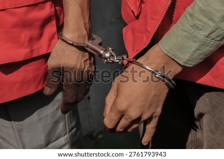 Two suspects in red vests handcuffed together during a legal investigation or criminal court proceeding.