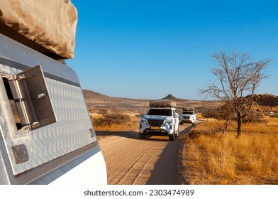 Two SUV 4x4 cars with rooftop tents driving in convoy through Spitzkoppe Park in Namibia.  Driving offroad at gravel road