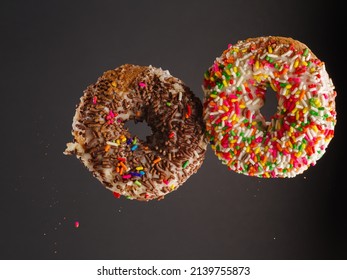 Two Sweet Colorful Donuts In A Frozen Flight On A Gray Background. There Are No People In The Photo. There Is Free Space To Insert. Invitation For A Holiday, Birthday.