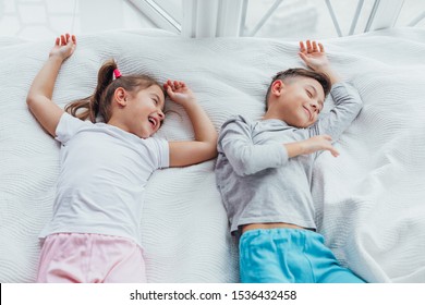 Two Sweet Kids Lying On Cozy Couch, Hands Over Head, Ready To Take A Nap.